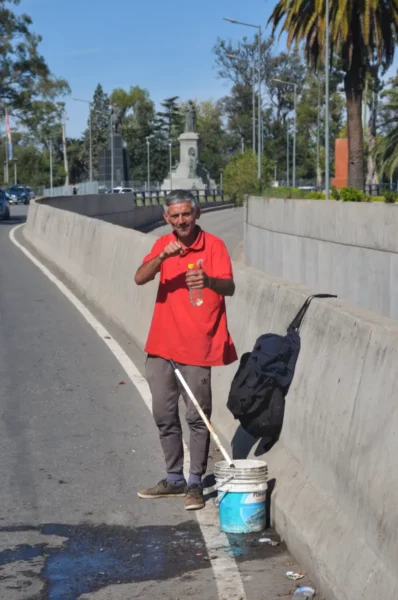 A man in a red shirt stands beside a busy road in Córdoba, Argentina, holding a bottle, with palm trees in the background.