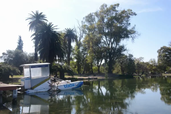 Serene waters reflect palm trees and greenery in Córdoba, Argentina, with a small boat moored at the dock under clear skies.