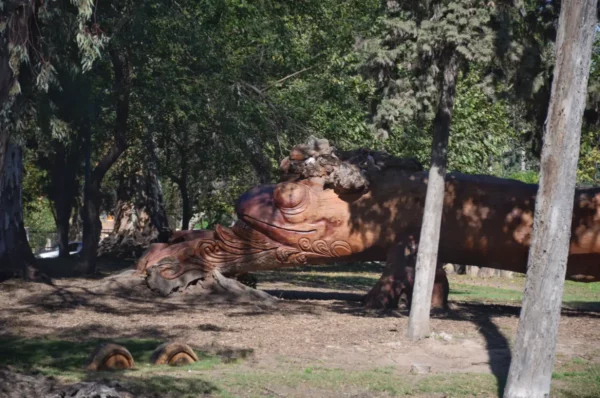 Giant dragon sculpture resting among trees in a park, showcasing intricate details amidst lush greenery in Córdoba, Argentina.