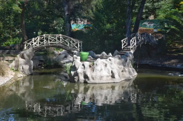 Serene rock formations and a wooden bridge reflect in the tranquil waters of a park in Córdoba, Argentina.