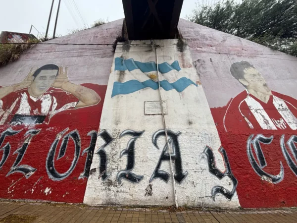 Mural featuring two football players with the Argentine flag, vibrant red and white colors, under a bridge in Córdoba, Argentina.