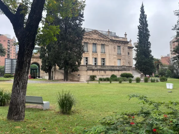 Elegant architecture with a stately facade and lush greenery, set in a park in Córdoba, Argentina. Overcast skies create a serene atmosphere.