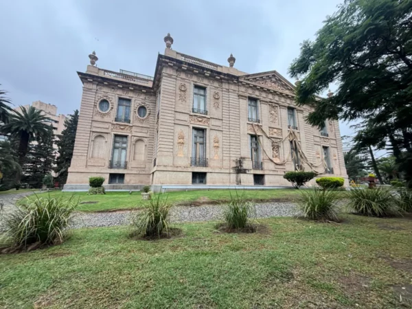 Elegant pink building with ornate architecture, surrounded by manicured gardens in Córdoba, Argentina. Overcast sky above.