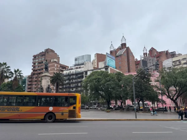 Vibrant Cordoba cityscape featuring a colorful bus, modern buildings, and lush trees under a cloudy sky in Argentina.