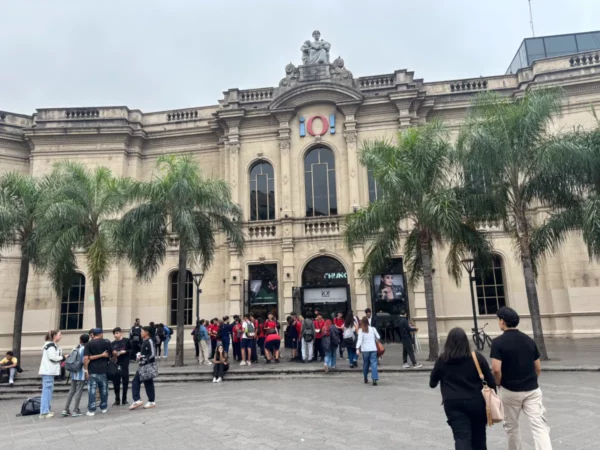 Palms frame the grand architecture of a historic building in Córdoba, Argentina, bustling with visitors in red shirts.