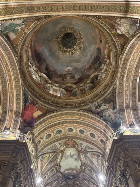 Intricate frescoes and ornate architecture adorn the ceiling of a historic building in Córdoba, Argentina, showcasing vibrant colors and detailed craftsmanship.