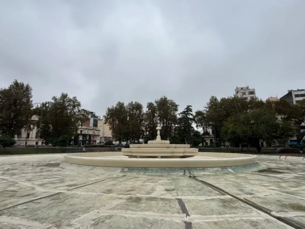 Elegant fountain surrounded by trees and buildings in Córdoba, Argentina, under a cloudy sky.