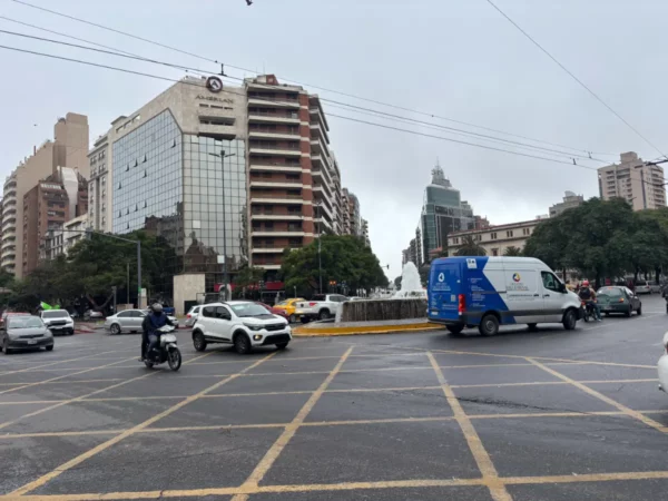 Traffic bustling on a rainy day in Córdoba, Argentina, featuring modern buildings and a central fountain amid green trees.