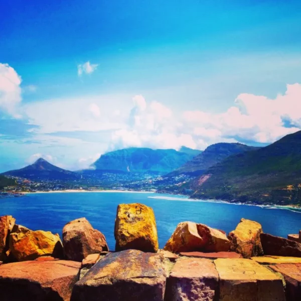 Vibrant blue waters and rocky shores frame the stunning landscape of Hout Bay, surrounded by majestic mountains under a clear sky.