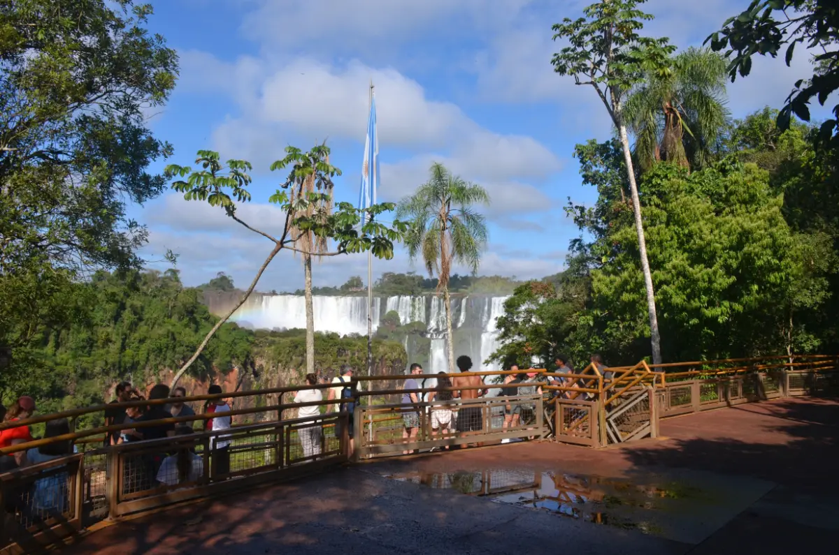 people marveling at iguazu falls from viewpoint with argentinian flag