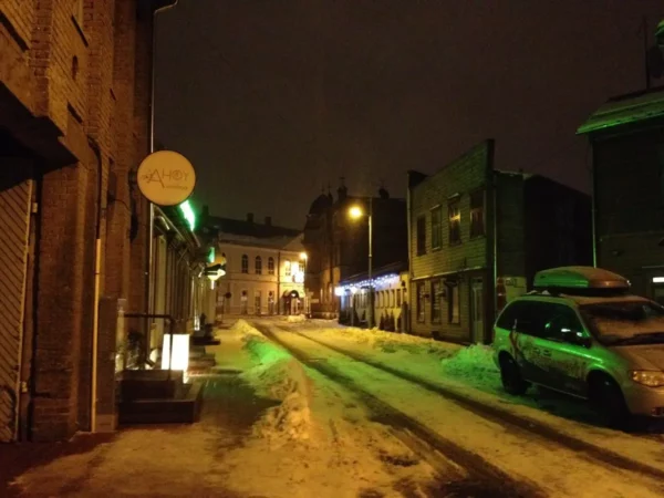 Snow-covered street illuminated by green and warm lights, highlighting the charming architecture of Pärnu at night.