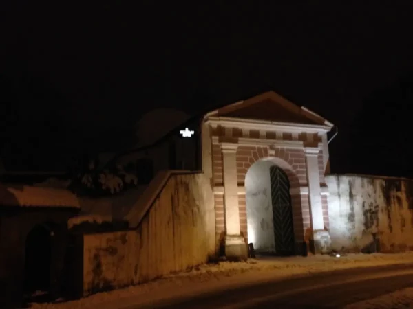 Historic building illuminated at night surrounded by snow in Pärnu, showcasing architectural details and a striking entrance.