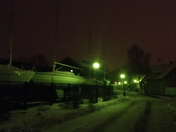 Boats lined up in a snowy harbor under greenish street lamps during a night scene in Parnu.