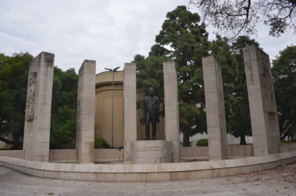 Statue surrounded by stone pillars in a park setting, with green trees and overcast skies in Rosario, Santa Fe, Argentina.