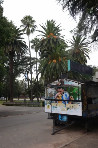 Colorful street art decorates a food cart, surrounded by lush palm trees in Rosario, Santa Fe, Argentina.