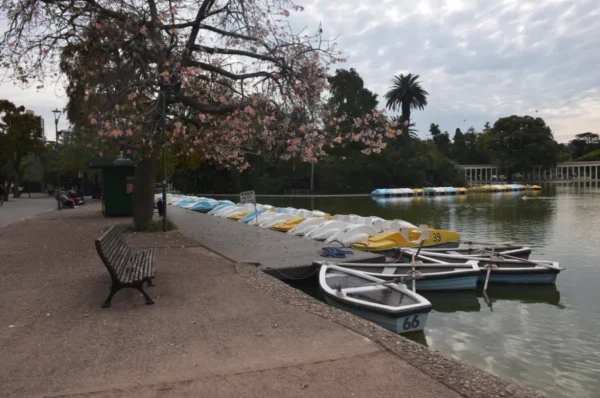 Colorful boats line the dock beside a tranquil lake in Rosario, Santa Fe, Argentina, with blooming trees and a serene park backdrop.