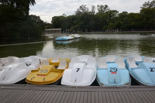 Colorful paddle boats lined up along the waterfront in Rosario, Santa Fe, Argentina, with lush greenery reflecting in the calm water.