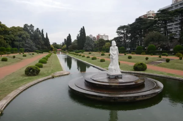 Elegant white statue on a circular platform surrounded by a manicured garden and reflecting water in Rosario, Santa Fe, Argentina.