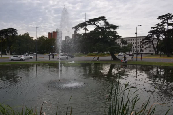 Fountain spraying water into a pond surrounded by lush greenery in Rosario, Santa Fe, Argentina, under a cloudy sky.
