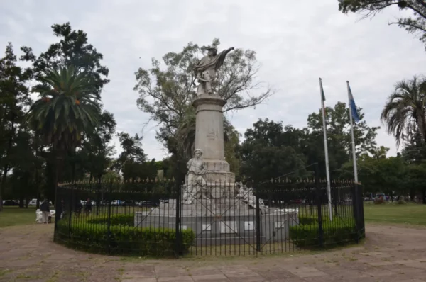 Monument topped with an eagle surrounded by greenery, fences, and flags in Rosario, Santa Fe, Argentina.