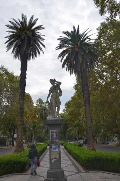 Statue surrounded by palm trees and lush greenery in Rosario, Santa Fe, Argentina. Cloudy sky adds to the serene atmosphere.