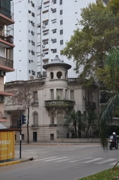 Elegant historic building with a turret stands at a street corner, surrounded by modern high-rises in Rosario, Santa Fe, Argentina.