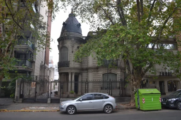 Historic architecture features a domed house beside a green garbage bin, framed by trees on a street in Rosario, Santa Fe, Argentina.
