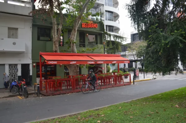 Bright red outdoor seating at a café lines the sidewalk in Rosario, Santa Fe, Argentina, surrounded by green trees and modern buildings.