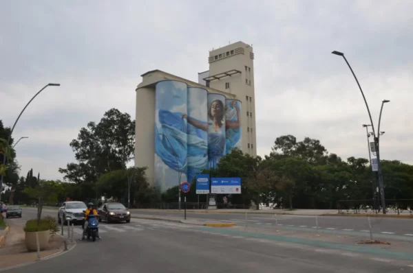 Vibrant street scene in Rosario, Santa Fe, showcasing a large mural on a building with greenery and traffic in the foreground.