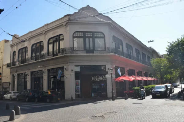 Historic building with balconies and awnings, surrounded by greenery and outdoor seating in Rosario, Santa Fe, Argentina.