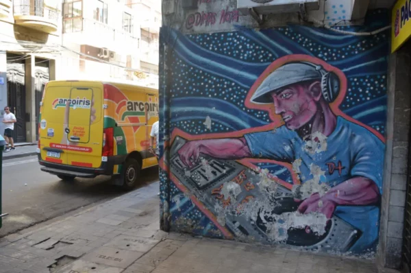 Vibrant street art depicting a DJ with headphones on a wall, with a colorful delivery van in Rosario, Santa Fe, Argentina.