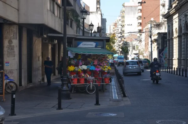Colorful flower stall along a street in Rosario, Santa Fe, Argentina, with buildings and parked vehicles in the background.
