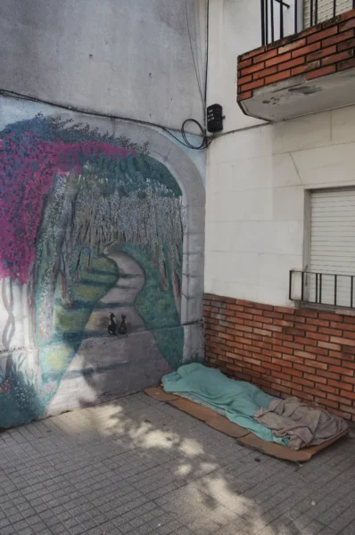 Vibrant mural depicting a tree-lined path alongside a textured wall, with a wooden platform for rest in Rosario, Santa Fe.