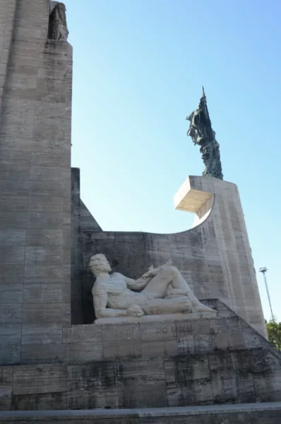Monument featuring a reclining figure and an imposing statue against a clear blue sky in Rosario, Santa Fe, Argentina.