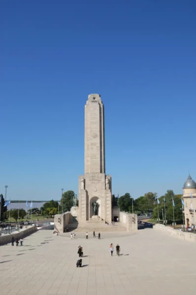 The towering monument stands against a clear blue sky in Rosario, Santa Fe, with visitors strolling around the plaza.