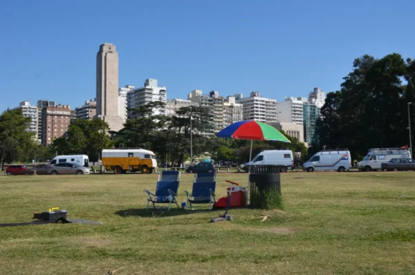 Colorful beach umbrellas shade empty chairs on a grassy area with city buildings in the background in Rosario, Santa Fe, Argentina.