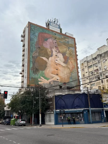 Vibrant mural on a tall building in Rosario, showcasing colorful figures against a cloudy sky in Santa Fe, Argentina.