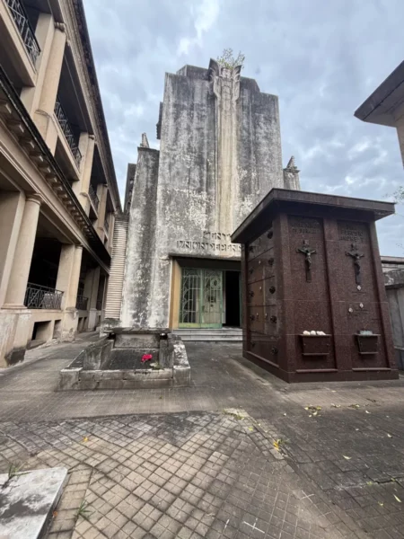 Cemetery in Rosario, Santa Fe, Argentina features a tall, weathered mausoleum and ornate tombs surrounded by grey skies.