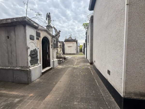 Quiet pathway lined with ornate tombs and mausoleums, set against a cloudy sky in Rosario, Santa Fe, Argentina.