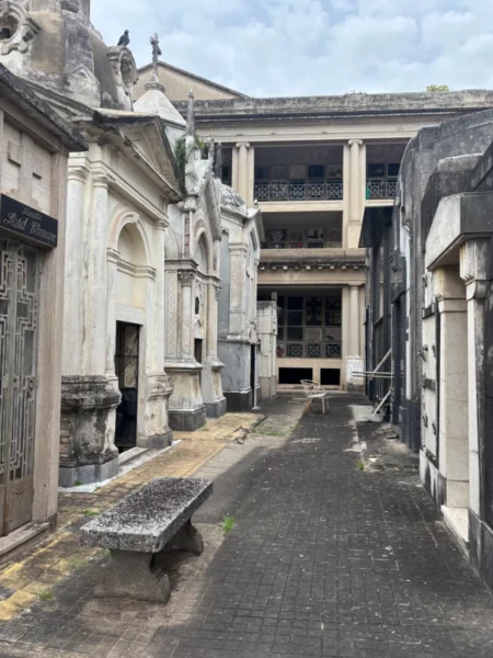Abandoned mausoleums and a stone bench line the path in a historic cemetery in Rosario, Santa Fe, Argentina.