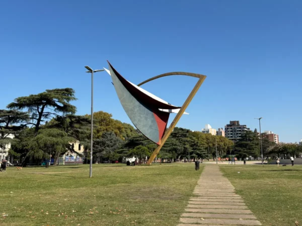 Stylized sculpture against a clear blue sky in Rosario, Santa Fe, Argentina, surrounded by greenery and pathways.