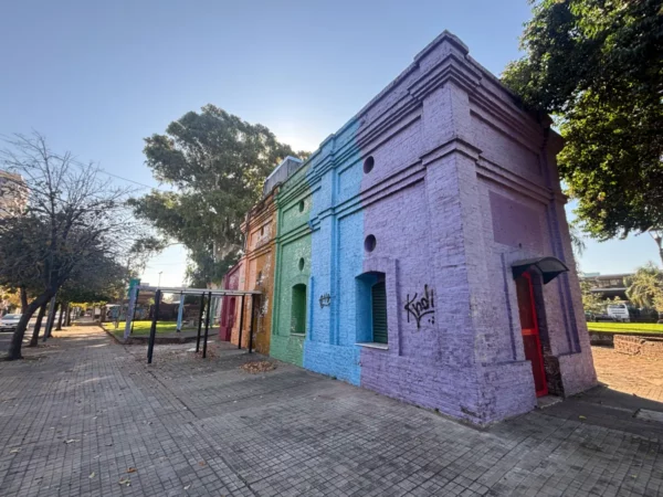 Colorful buildings clad in pastel hues stand on a sunny street in Rosario, Santa Fe, Argentina, with trees lining the walkway.