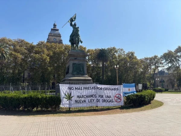 Equestrian statue surrounded by greenery in Rosario, Santa Fe, Argentina, with protest banners advocating for drug law reform.