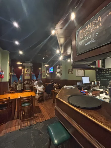 Rustic restaurant interior in Rosario, Santa Fe, Argentina, featuring wooden tables, warm lighting, and a chalkboard menu.