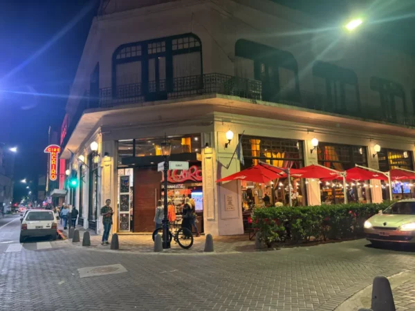 Vibrant night scene in Rosario, Santa Fe, Argentina, featuring a bustling restaurant with red umbrellas and lively street activity.