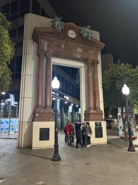 Historic archway adorned with sculptures, illuminating the night sky in Rosario, Santa Fe, Argentina, with people gathered below.