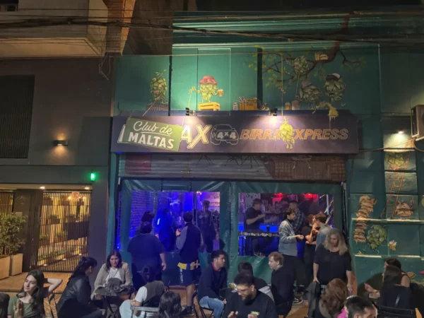 Vibrant nightlife scene at Club de Maltas in Rosario, Santa Fe, with patrons enjoying drinks outside under colorful neon lights.