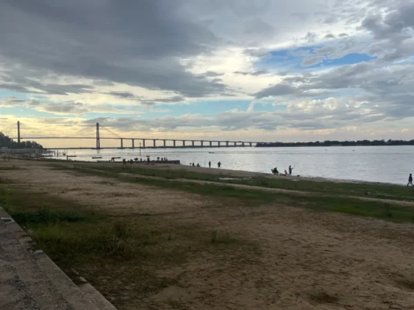 Golden sandy shorelines stretch along the Paraná River, with a bridge arching gracefully under a cloudy sky in Rosario, Santa Fe, Argentina.