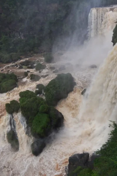 Powerful cascades of water flow over rugged terrain at Saltos del Monday Falls in Paraguay, surrounded by lush greenery.
