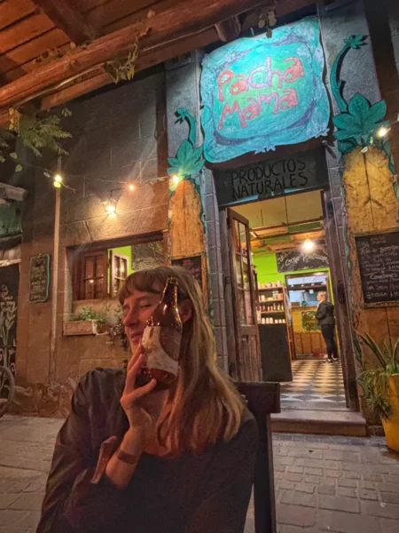 girl holding a beer bottle in a bar around the square of san marcos sierras hippie village in argentina